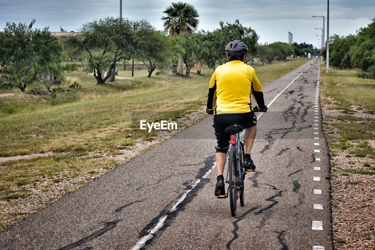 REAR VIEW OF GIRL RIDING BICYCLE ON ROAD