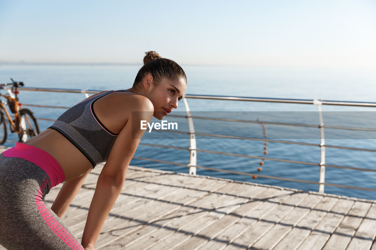 Young woman standing by railing against sea