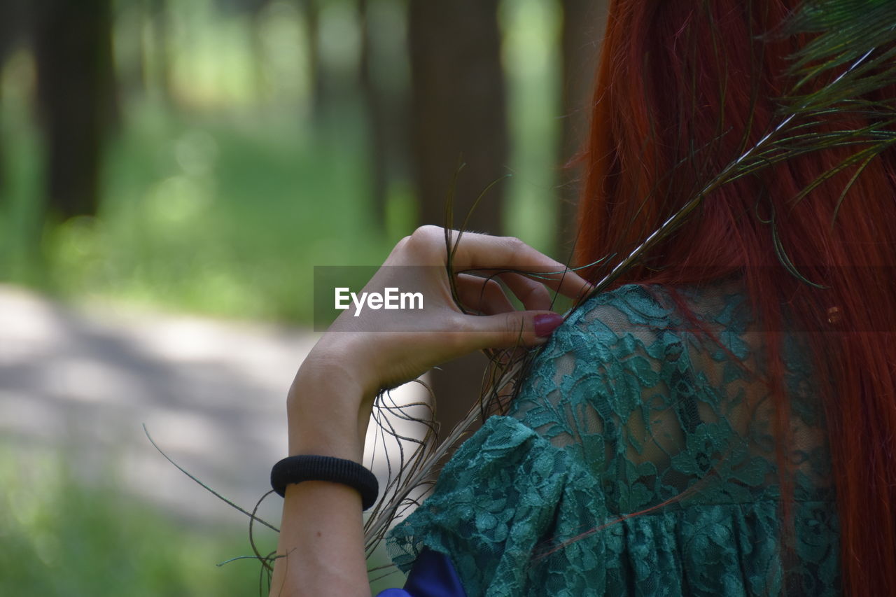 Midsection of woman holding peacock feather while standing outdoors