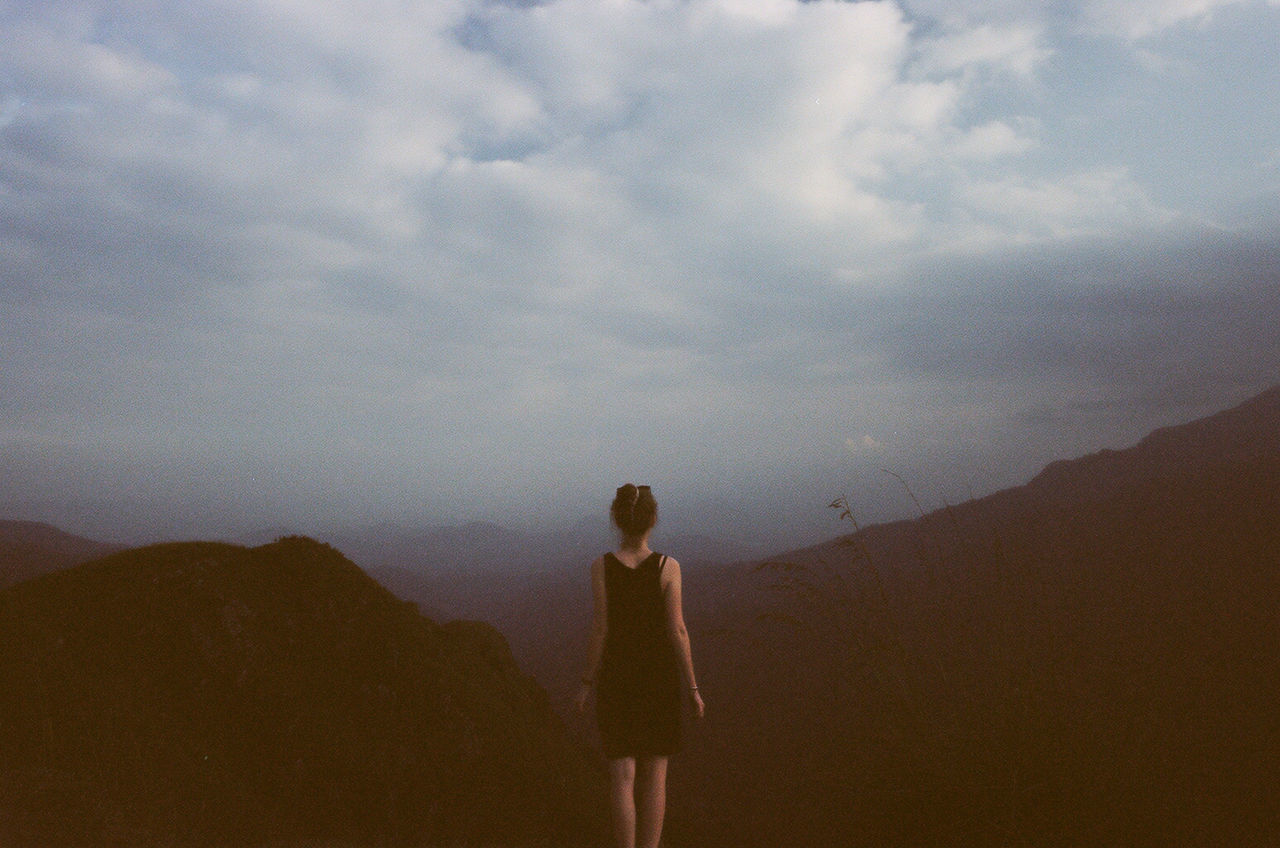 Rear view of woman standing on mountain against cloudy sky at dusk