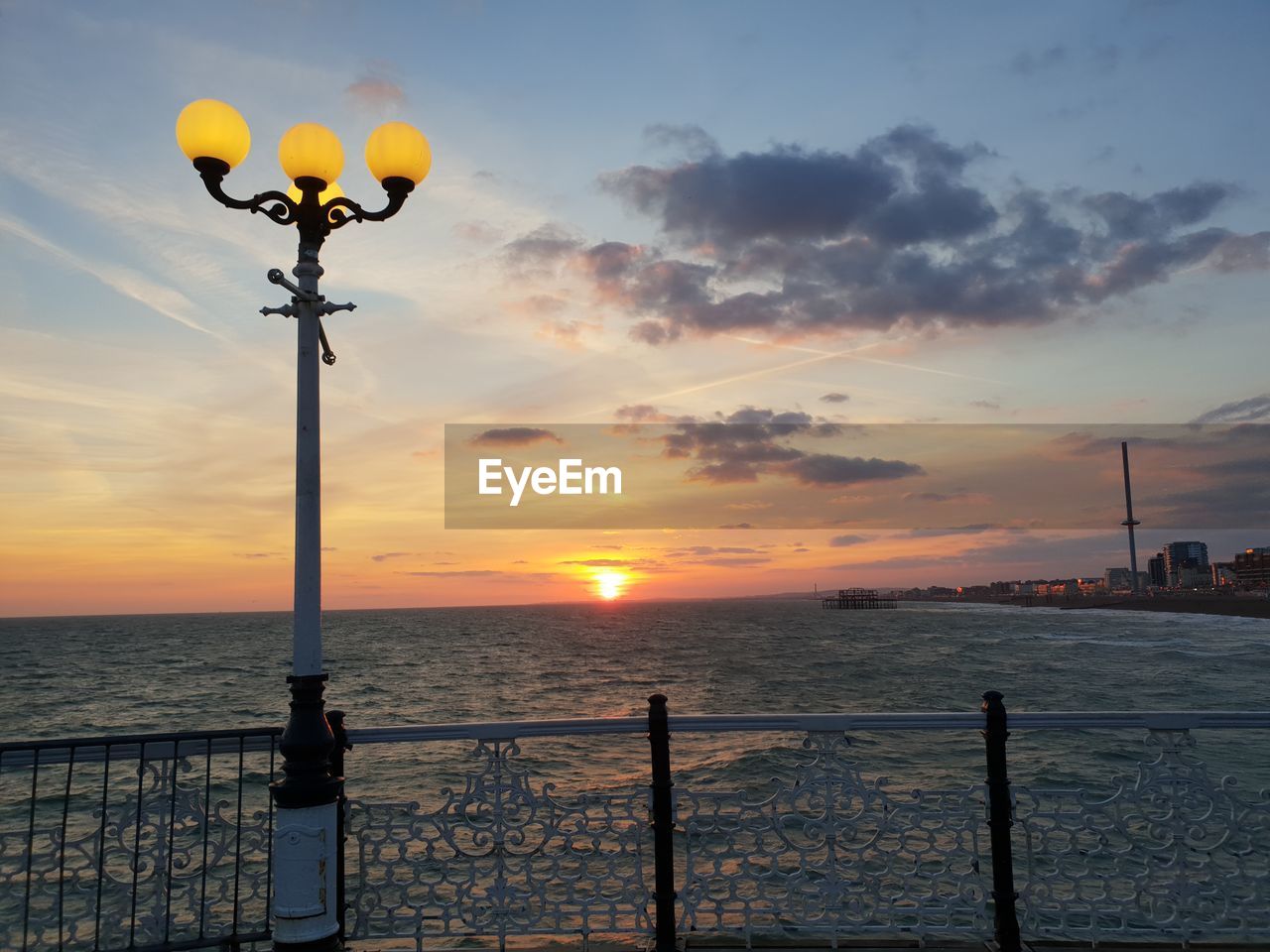 Street light by sea against sky during sunset