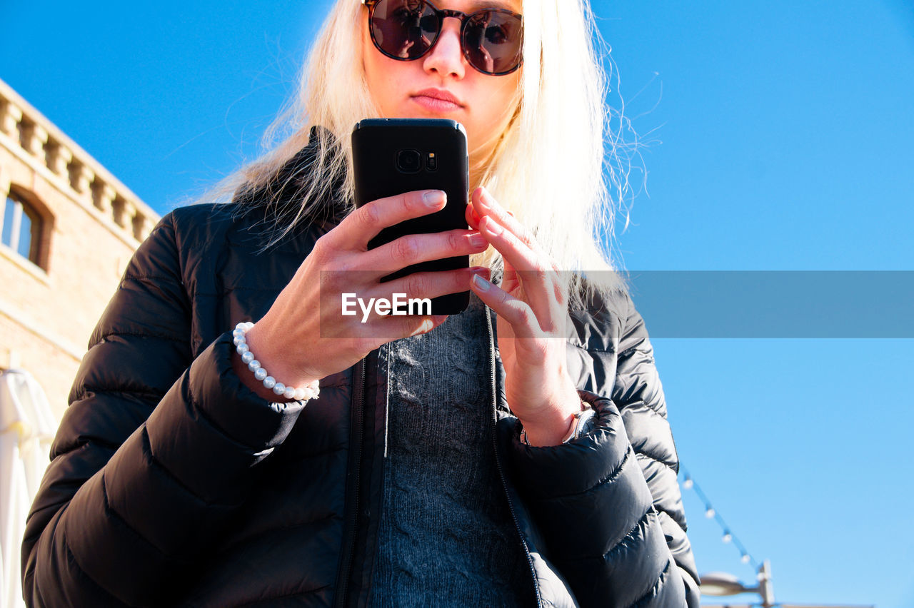 Low angle view of woman using phone against clear sky