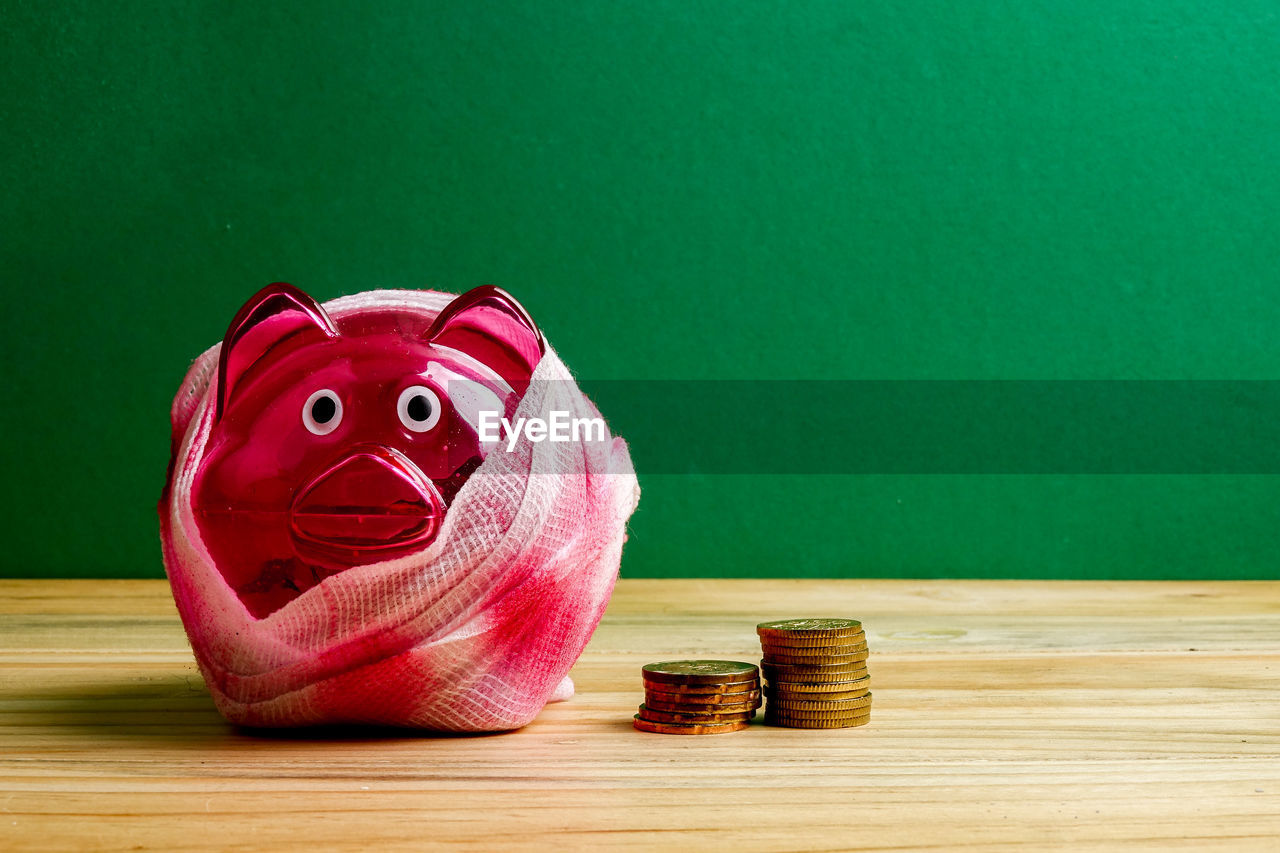 Close-up of wounded piggy bank wrapped in bandage on wooden table against green background