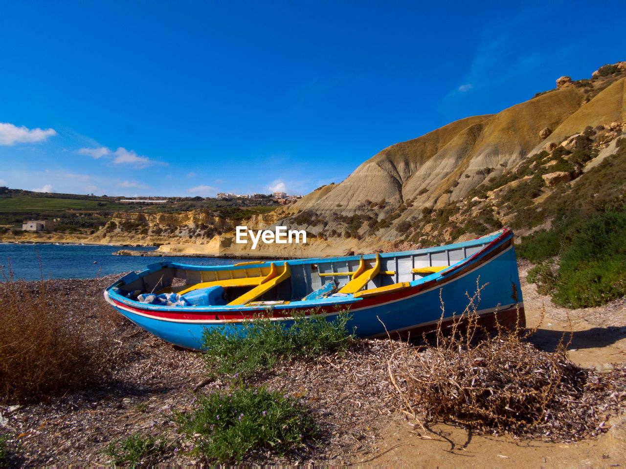 Boat moored on beach against blue sky