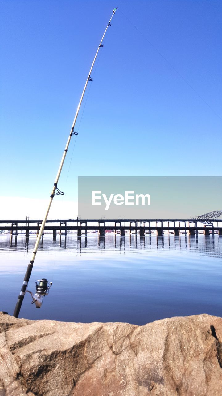 Scenic view of lake against clear blue sky with fishing pole