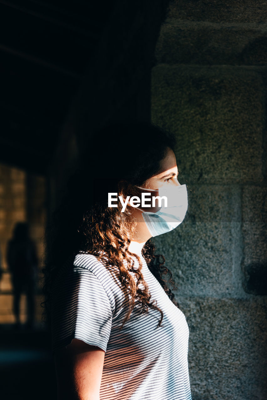 Side view of woman standing against window wearing face mask