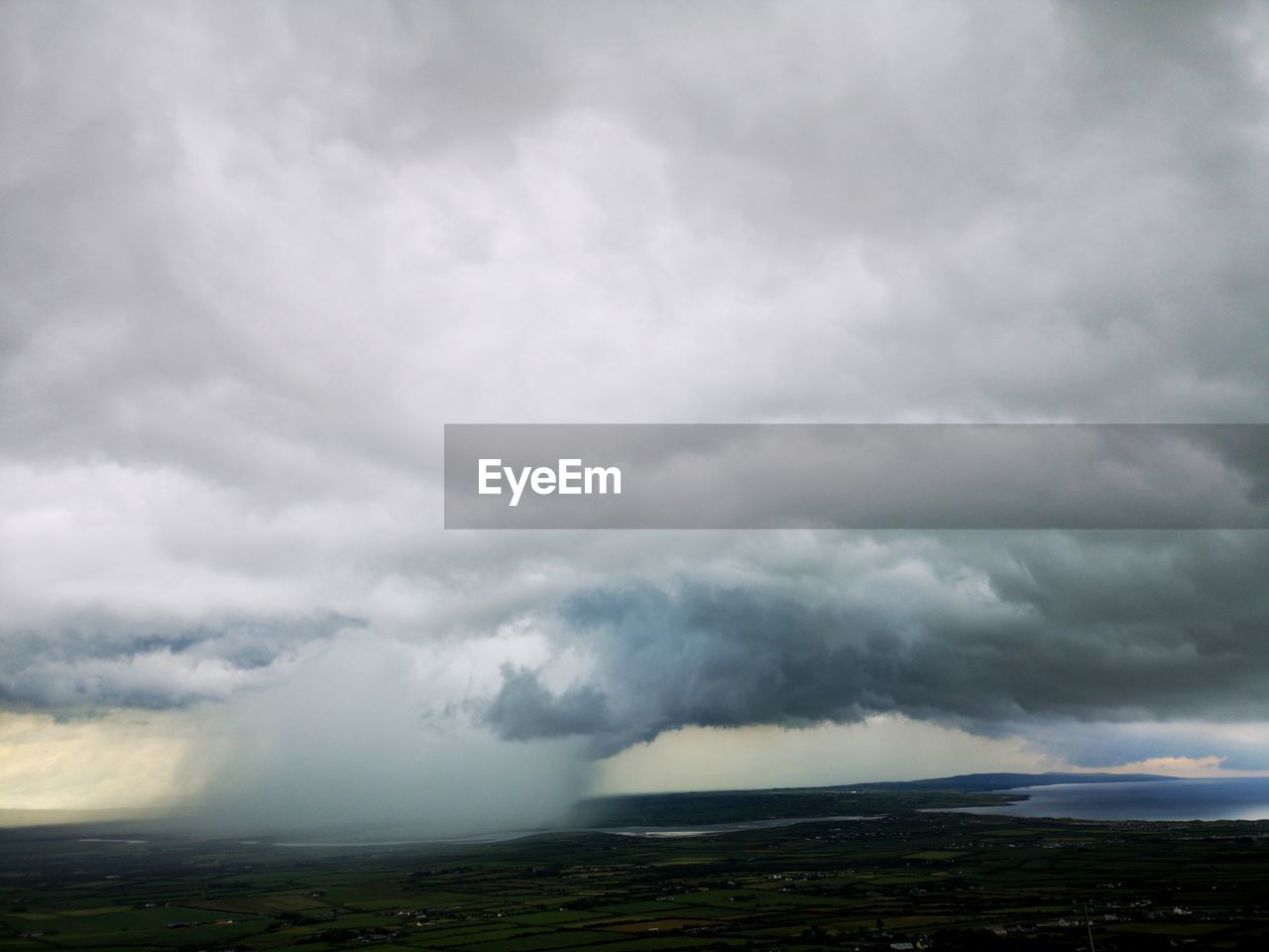 Storm clouds over land with cloudburst in distance.