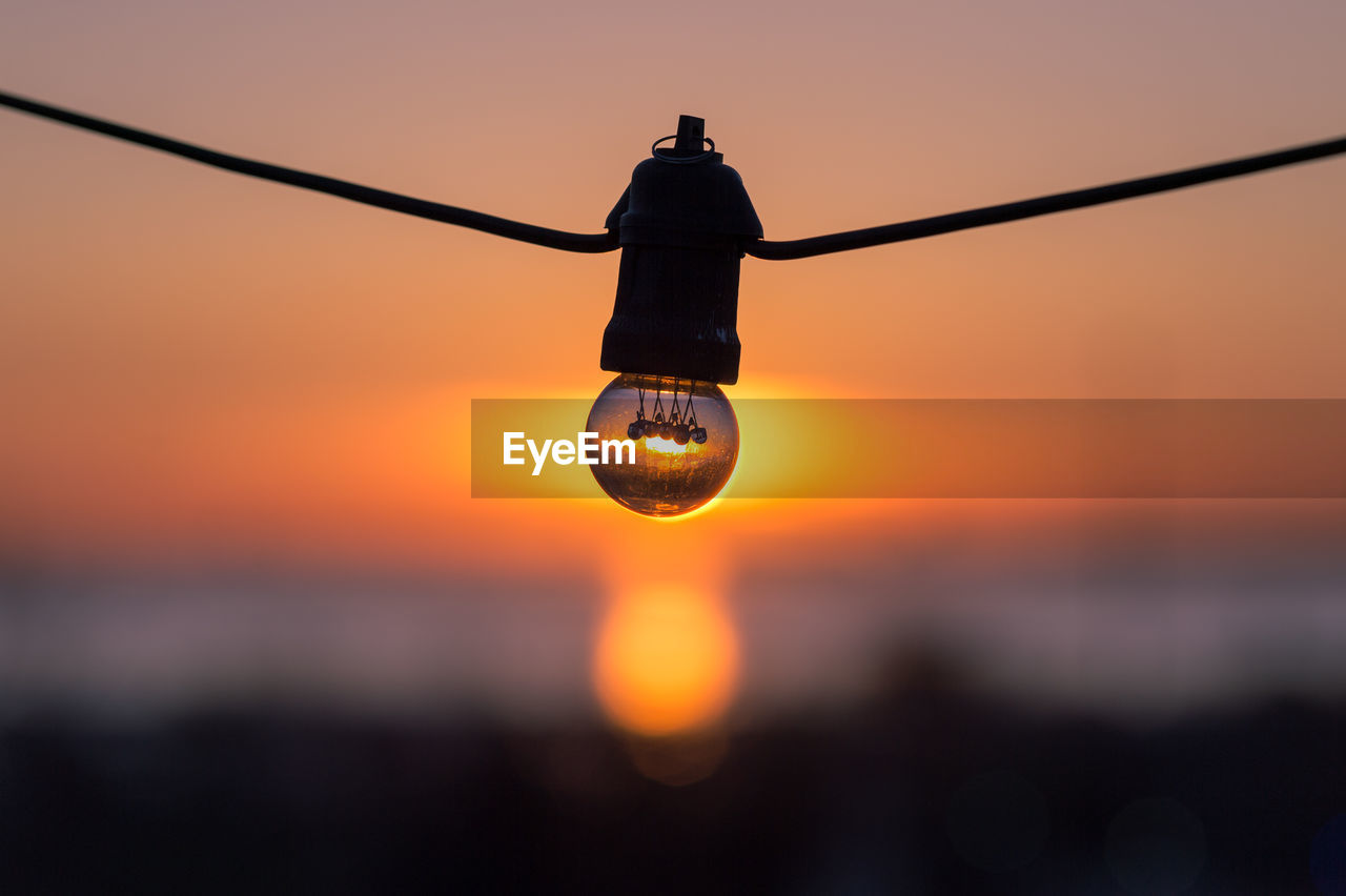 Close-up of light bulb against sky during sunset