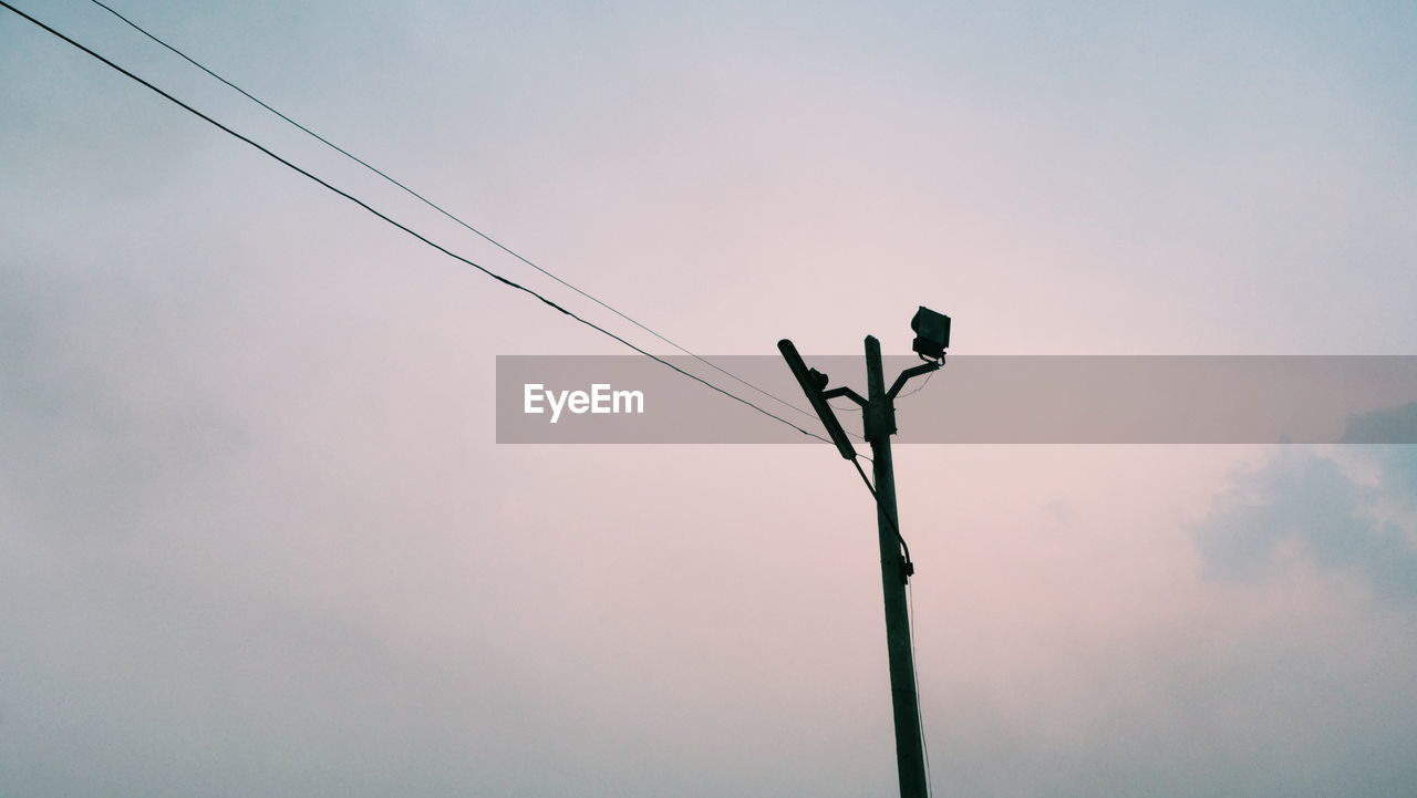 LOW ANGLE VIEW OF A BIRD PERCHING ON CABLE AGAINST SKY