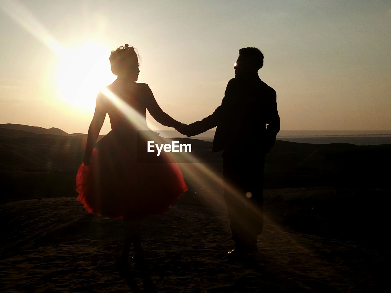 Couple holding hands against sky during sunset