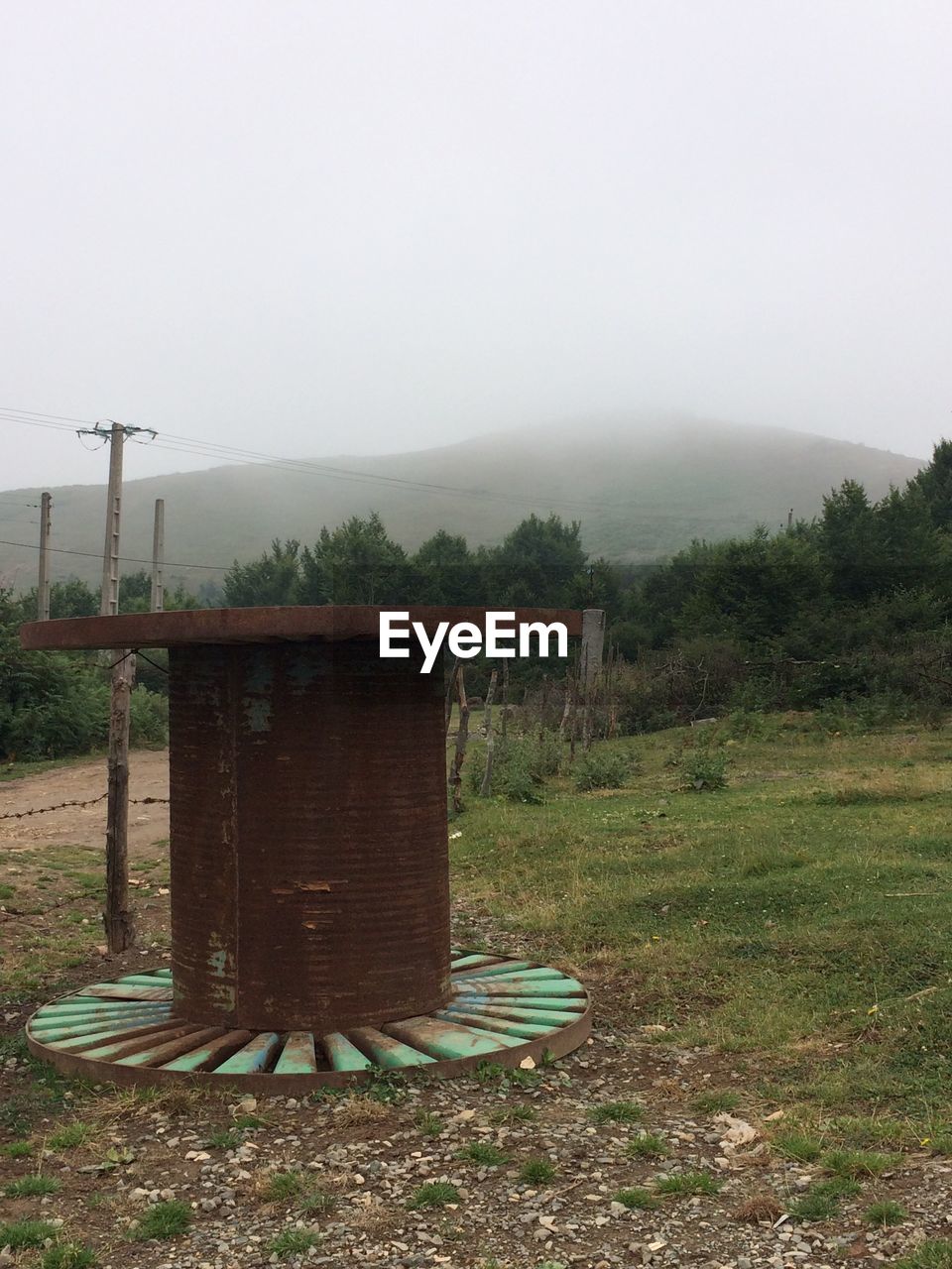 Rusty metallic spool on field against clear sky