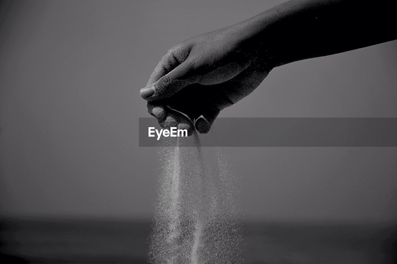 Cropped hand playing with sand at beach against sky