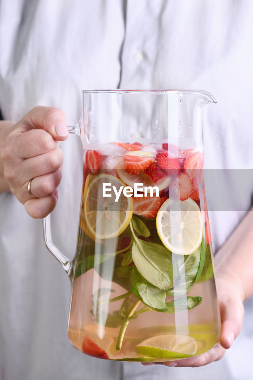 A jug with organic soft drink with ripe fresh strawberries, lemon slices with lime and basil, 