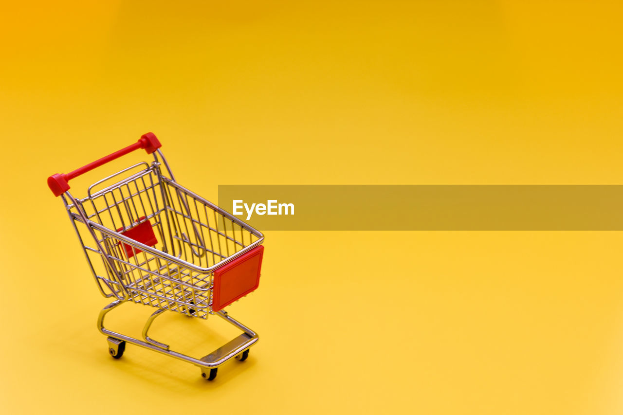 An empty mini supermarket cart on a yellow background.