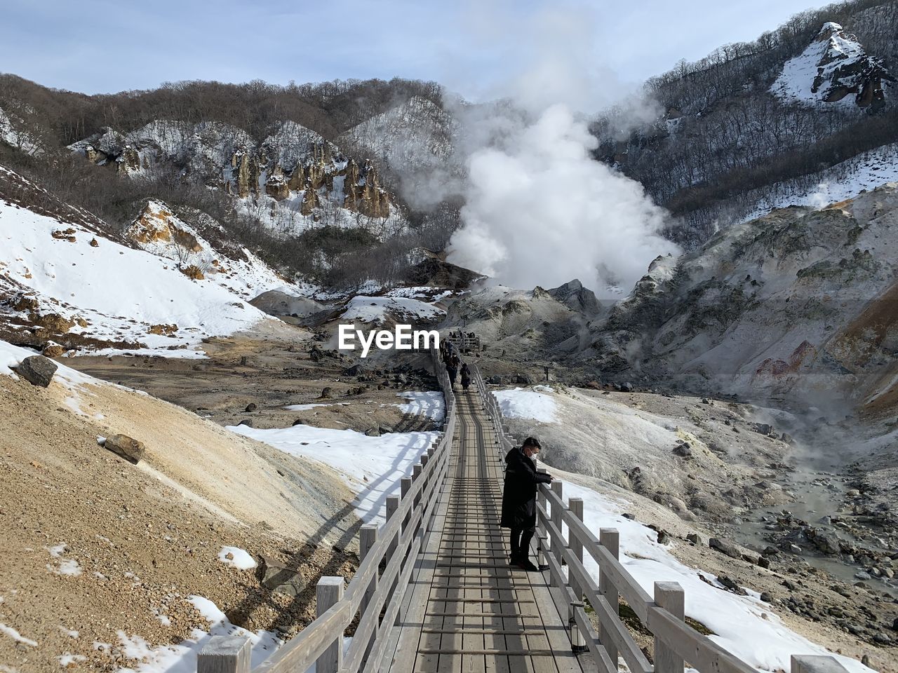 Man standing on boardwalk amidst mountain during winter