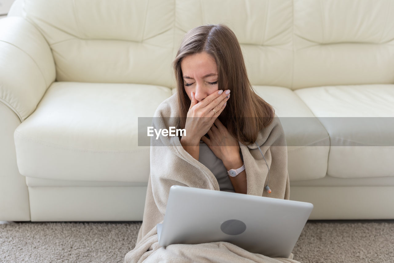 WOMAN USING MOBILE PHONE WHILE SITTING ON SOFA