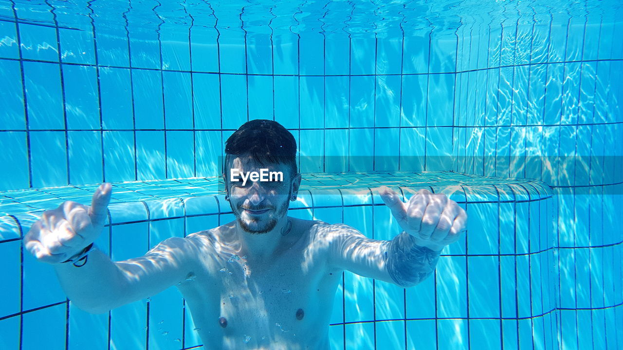 Portrait of shirtless young man gesturing thumbs up in swimming pool