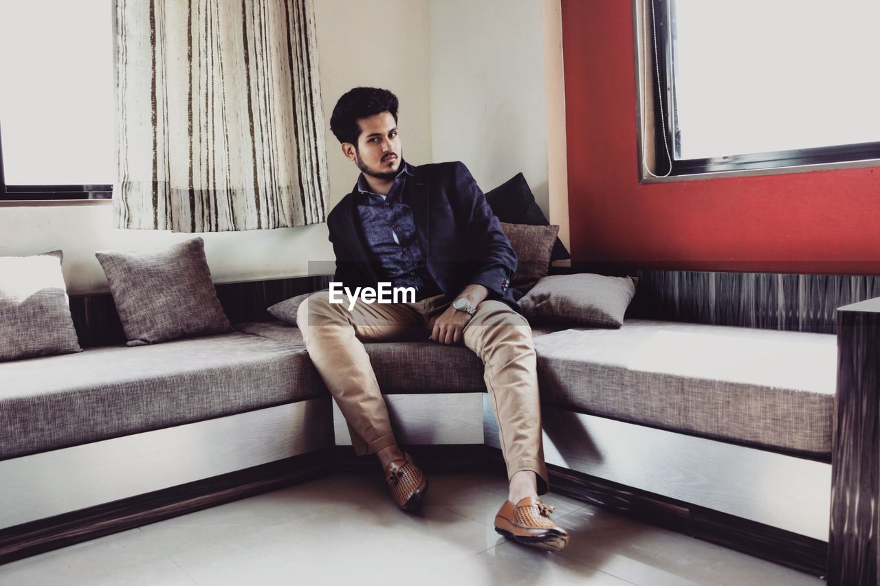 Full length portrait of young man sitting on sofa at home