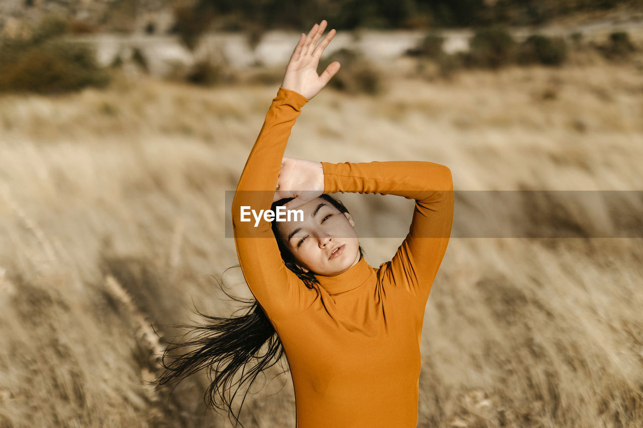 Beautiful woman with arms raised standing in field during windy day