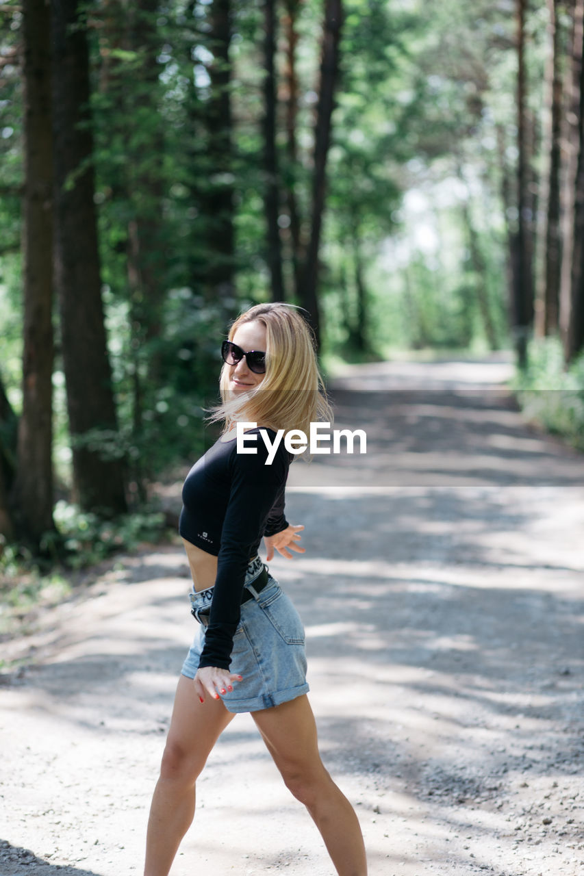 FULL LENGTH OF WOMAN WEARING SUNGLASSES IN FOREST