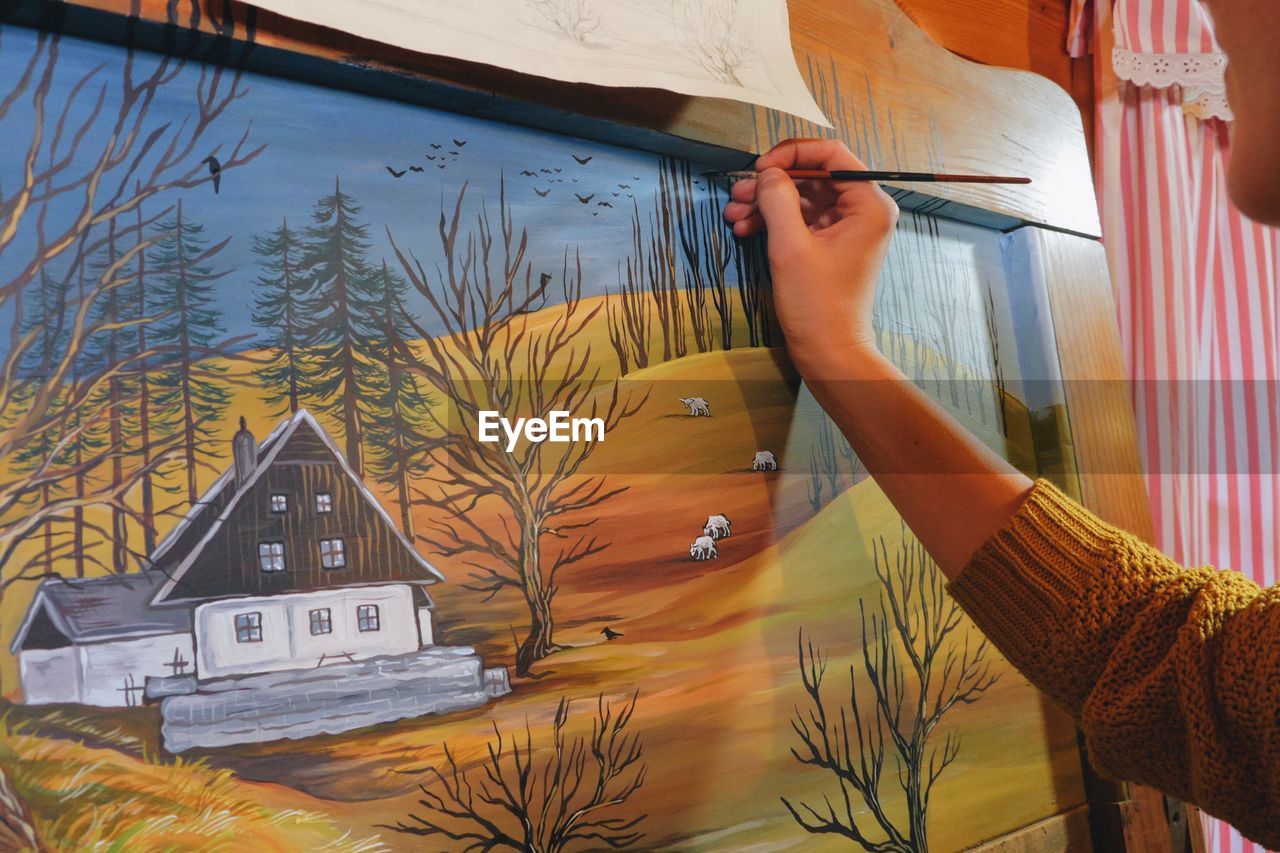 Cropped hand of woman drawing on canvas in cottage