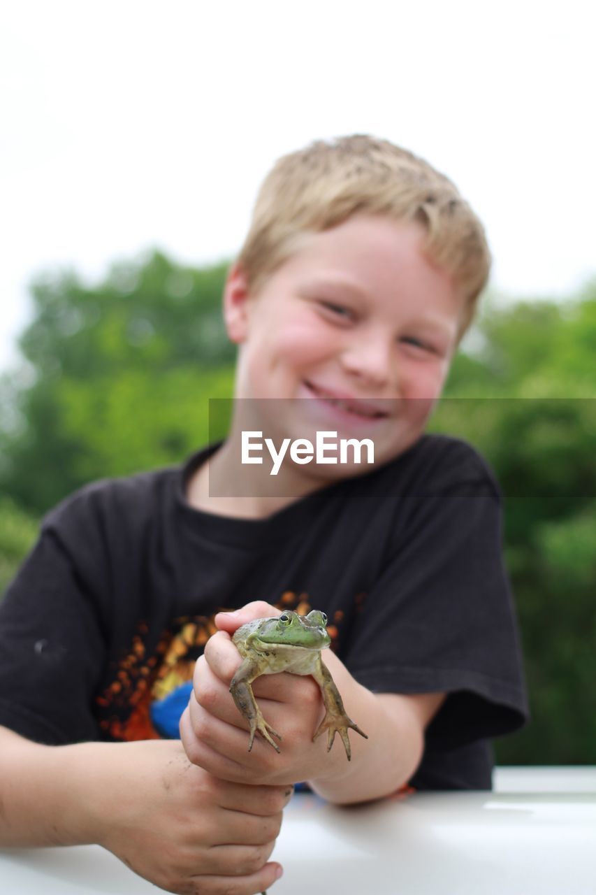 Portrait of smiling boy holding frog outdoors