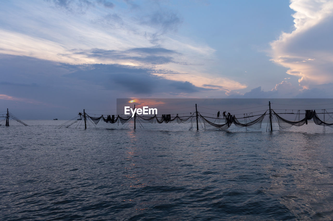 SCENIC VIEW OF WOODEN POSTS IN SEA AGAINST SKY DURING SUNSET