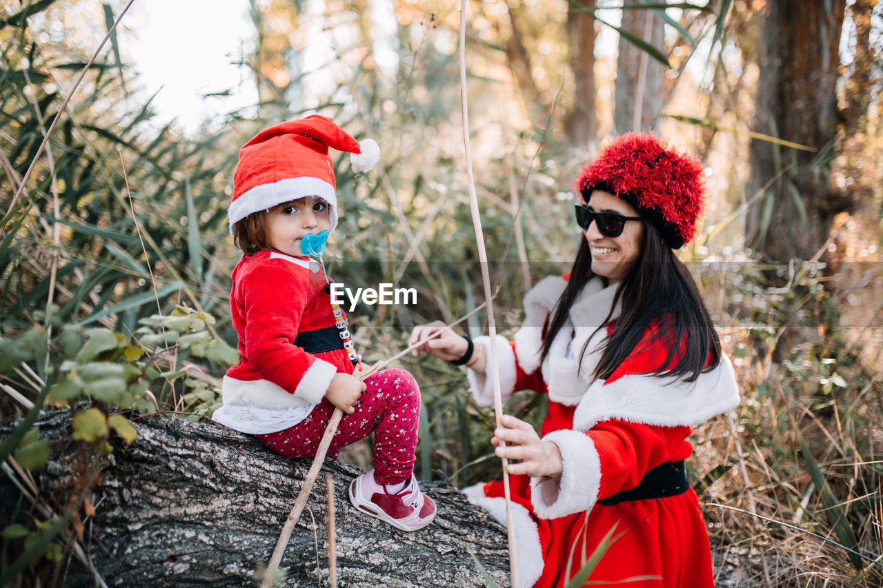 Cute baby girl with mother wearing santa costume in forest