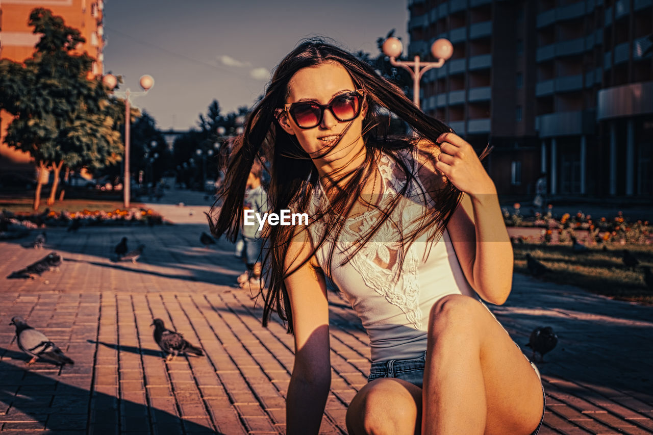 YOUNG WOMAN WEARING SUNGLASSES SITTING ON TRADITIONAL CLOTHING