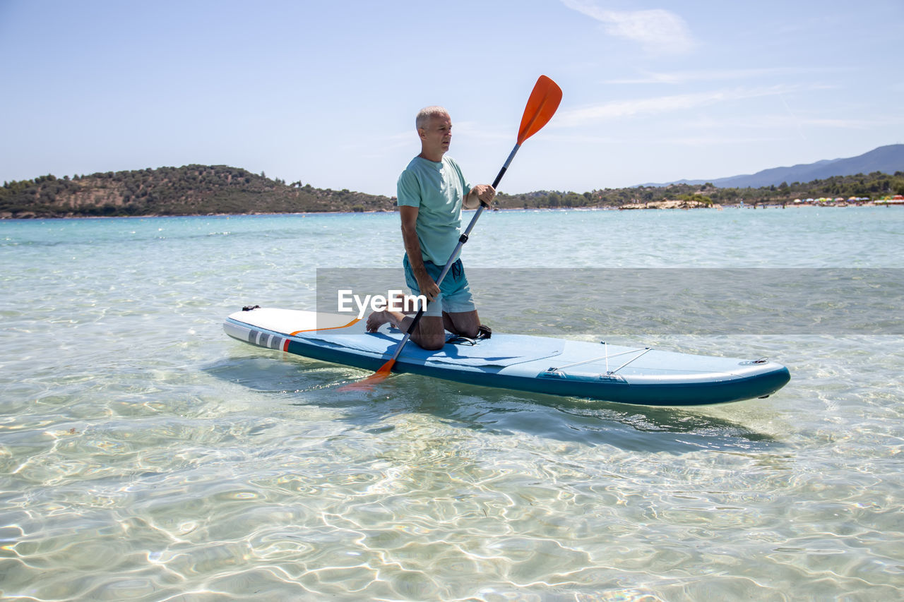 Sup surfing.beautiful view of the sea with a mature man kneeling on a board with paddle in the water