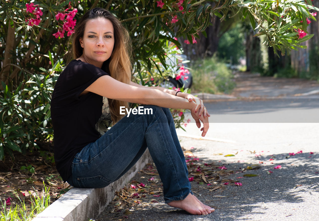 Portrait of young woman sitting on retaining wall by plants