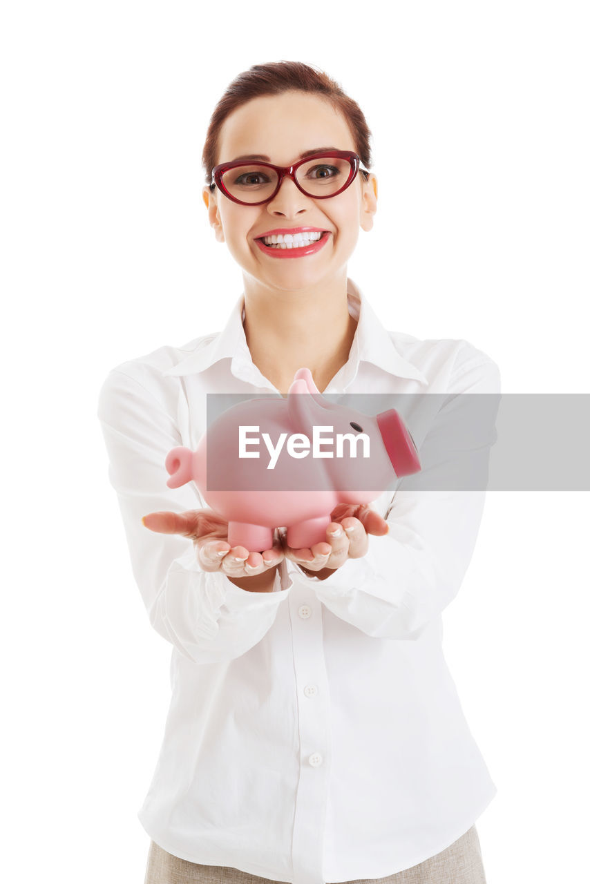 Portrait of smiling young businesswoman holding piggy bank against white background