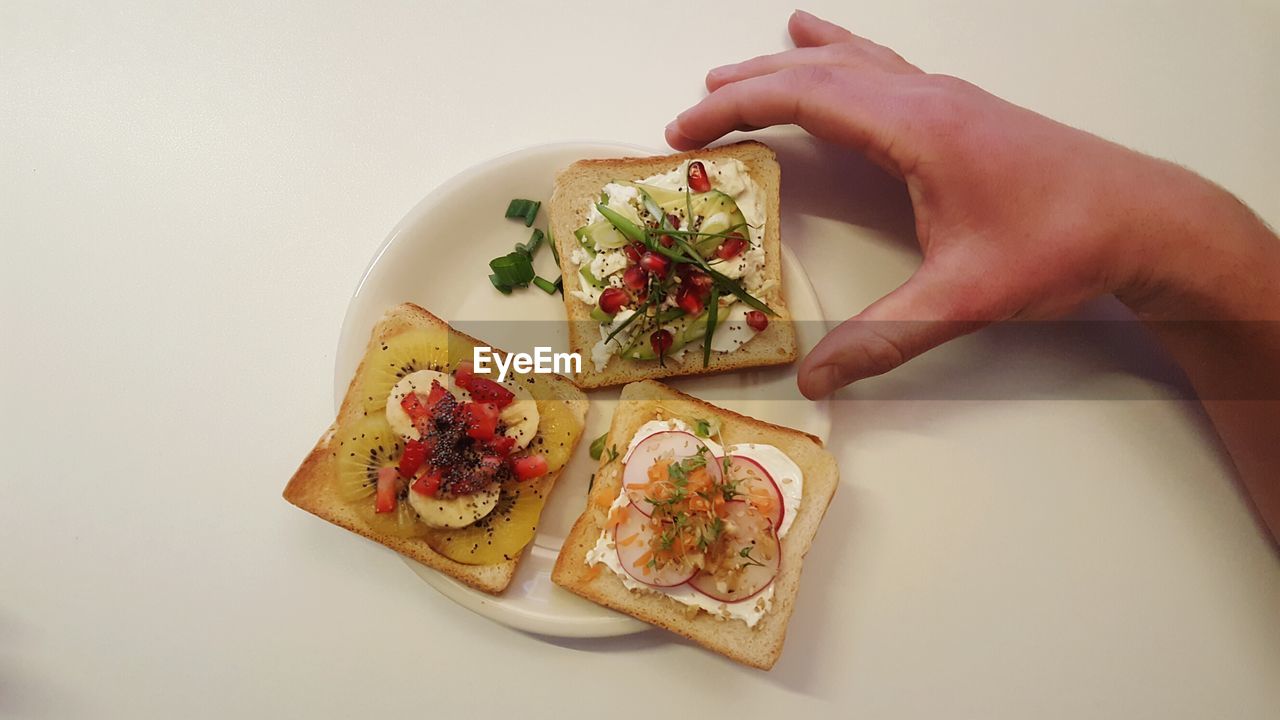 Cropped hand of man holding open faced sandwich in plate on white table