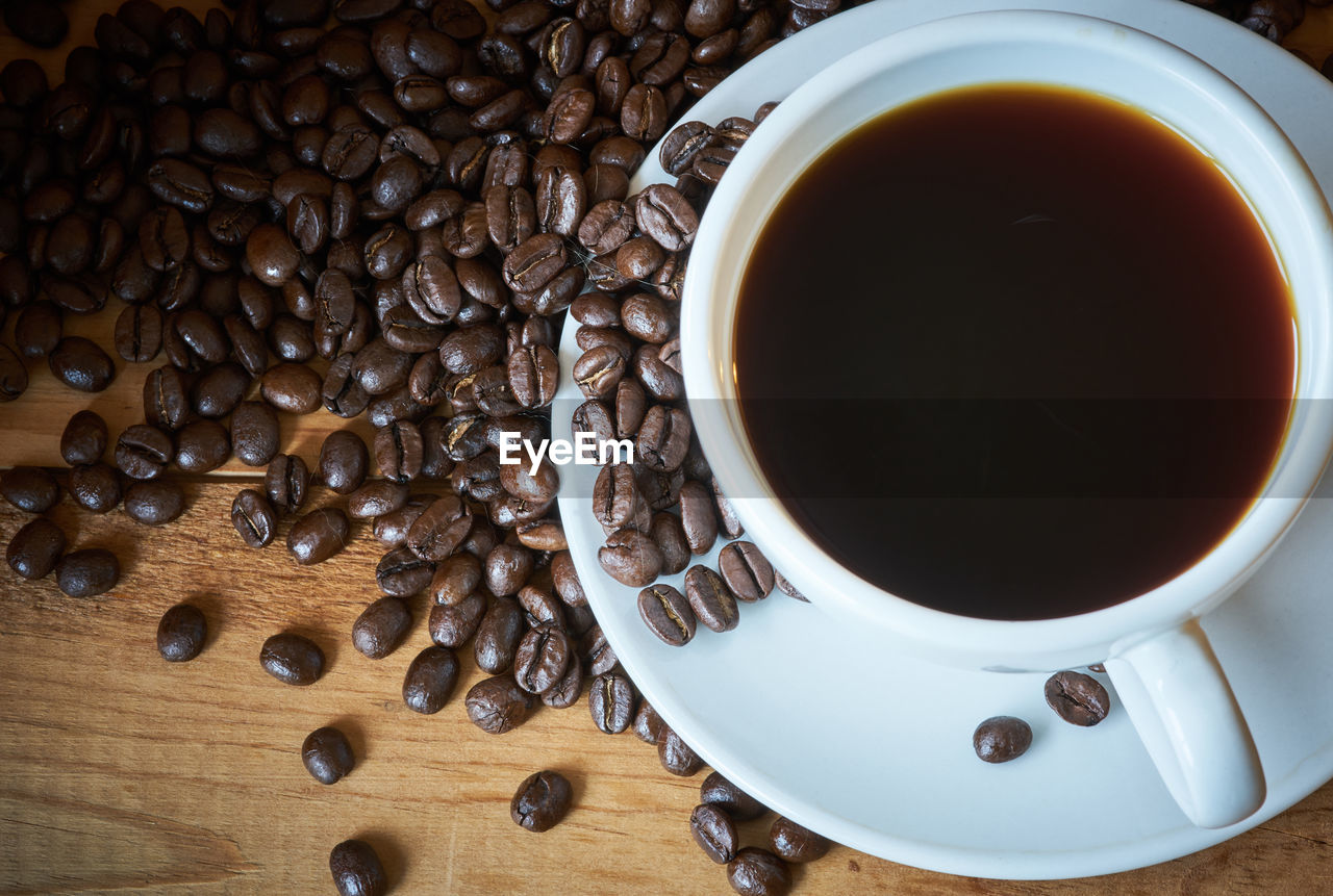 High angle view of coffee cup and roasted beans on table