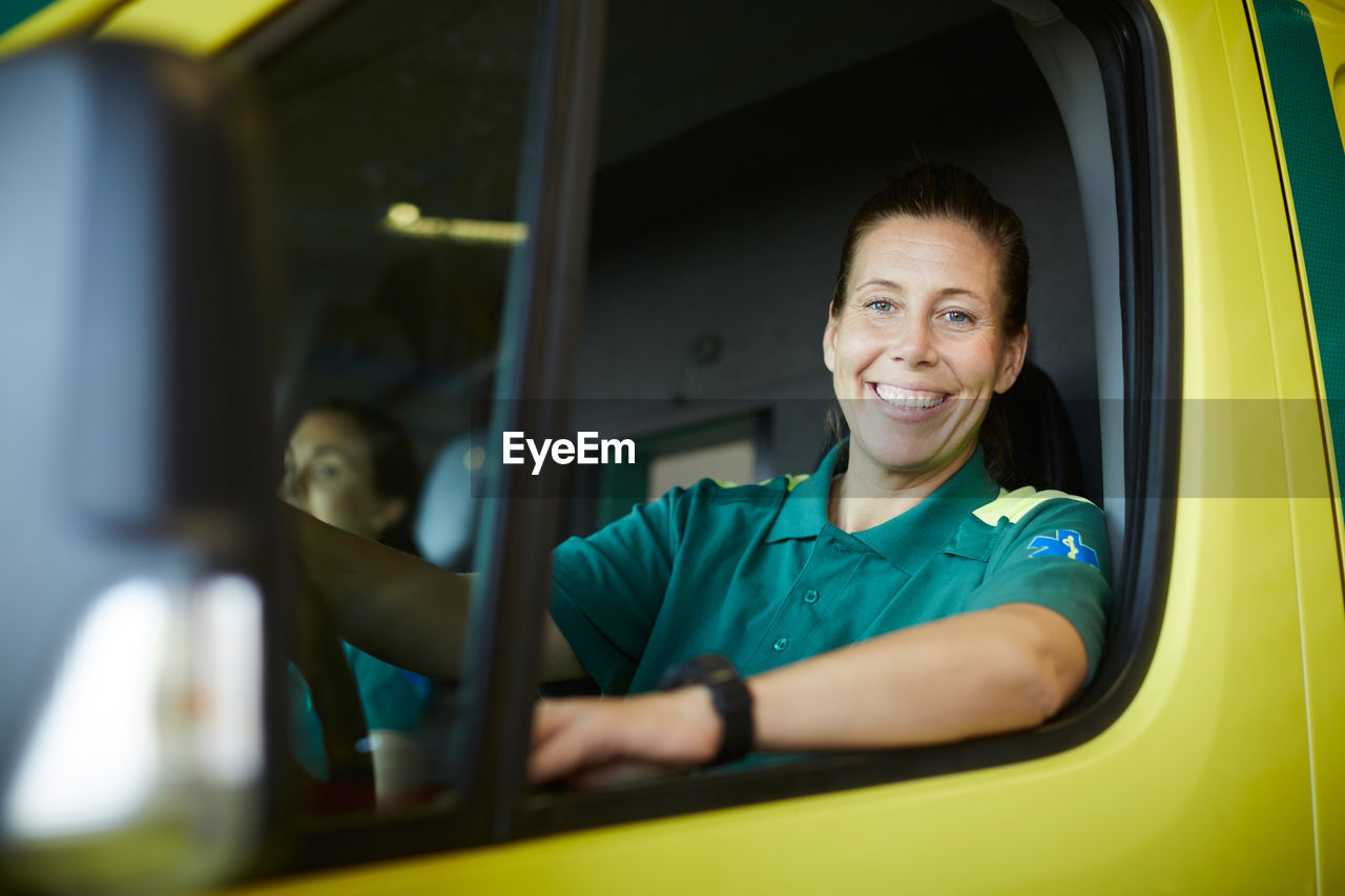 Portrait of smiling mature female paramedic driving ambulance in parking lot
