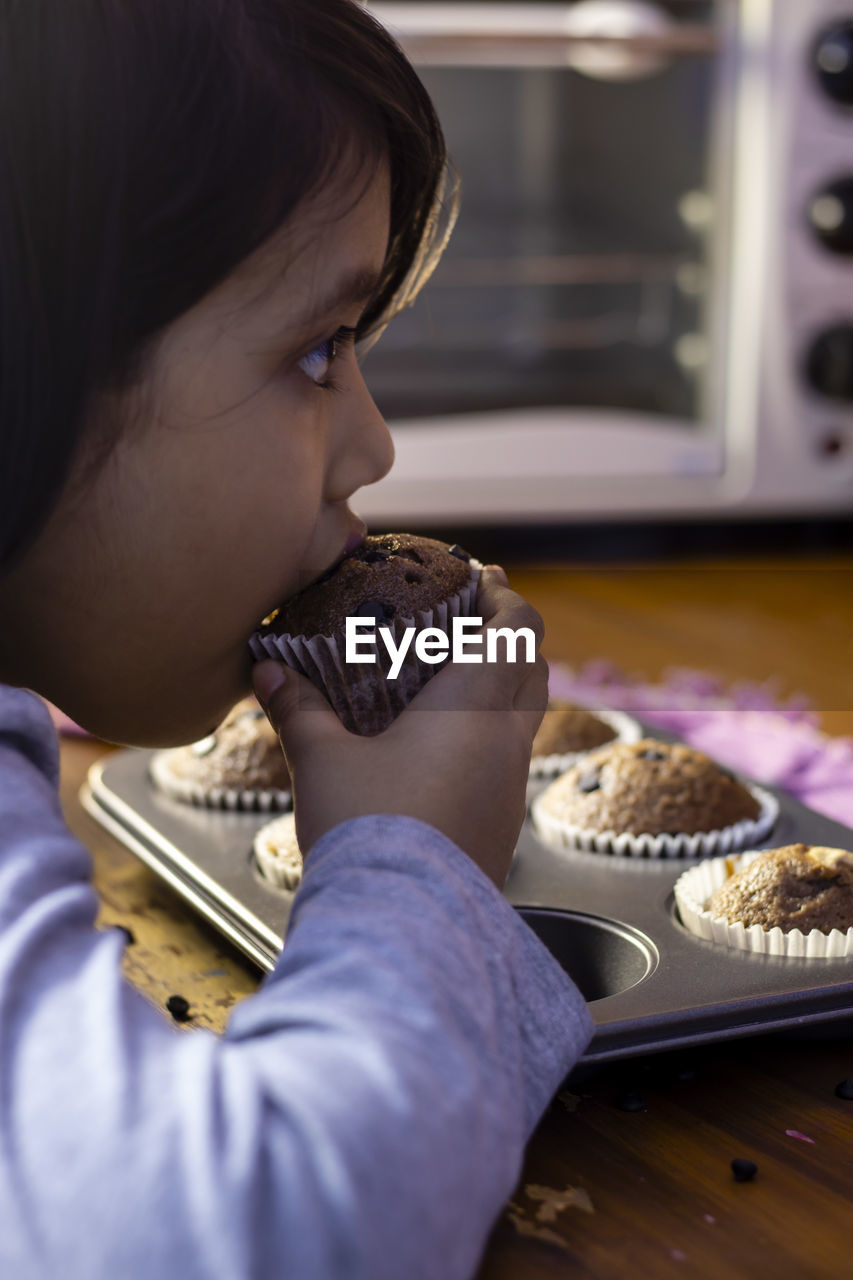 An indian girl child eating a homemade chocolate muffin cup cake baking tray with selective focus