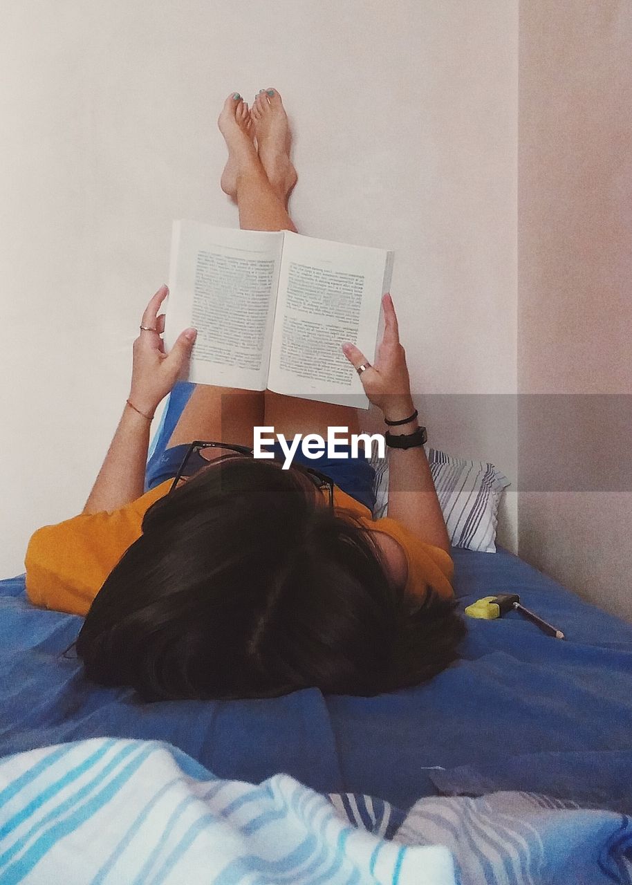 Woman reading book while lying on bed at home