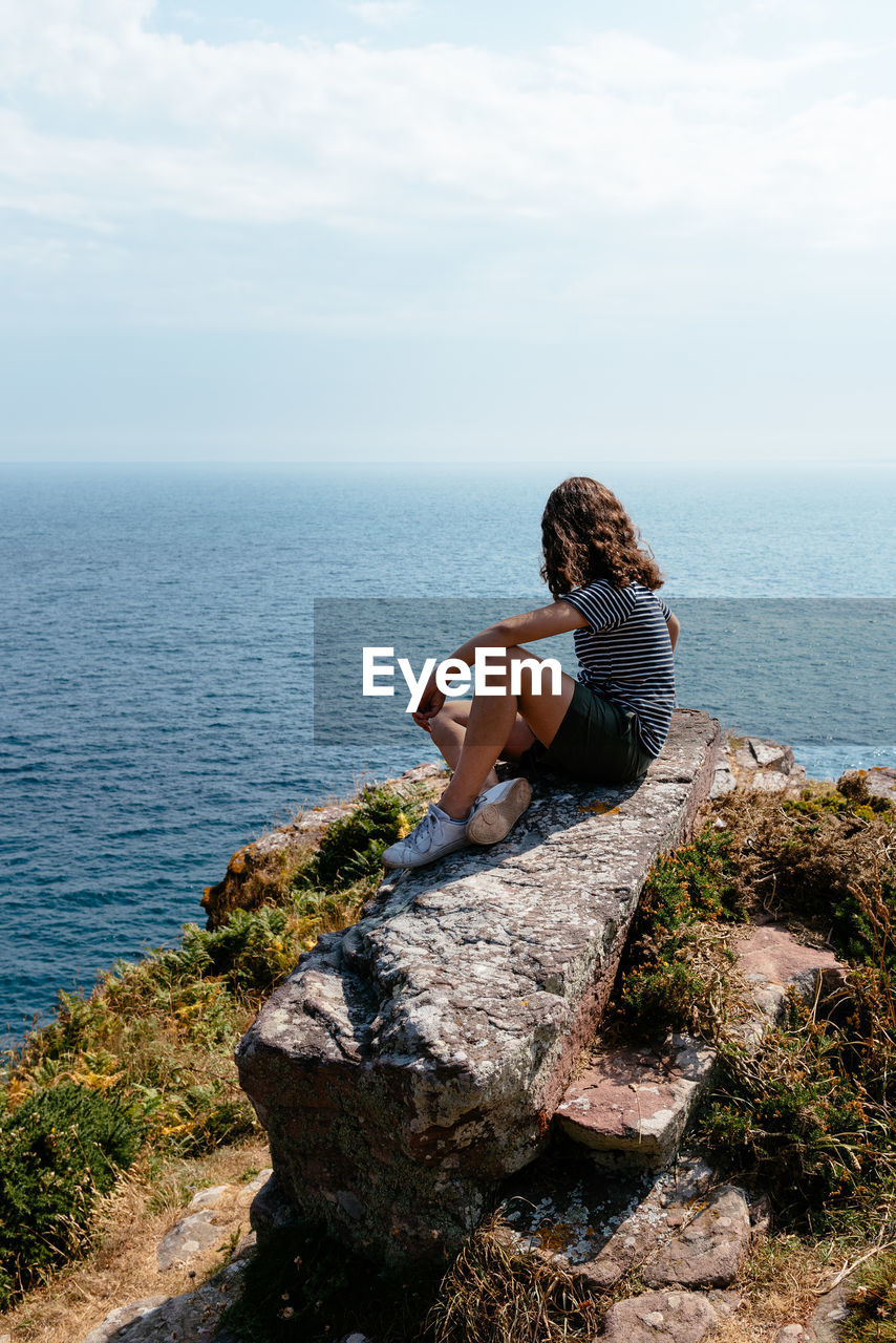 Man sitting on rock by sea against sky