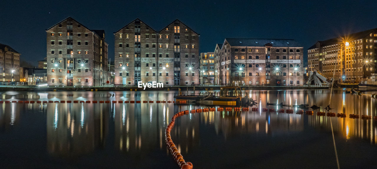 Illuminated buildings by lake against sky in city at night