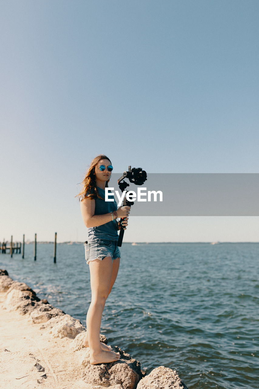 FULL LENGTH OF YOUNG WOMAN PHOTOGRAPHING SEA