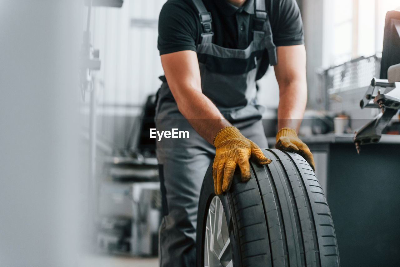 Close up view of wheel. man in uniform is working in the auto service.