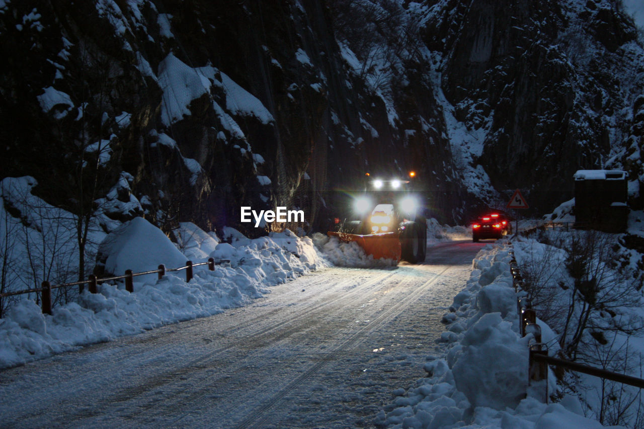 SNOW COVERED ROAD BY TREES AT NIGHT