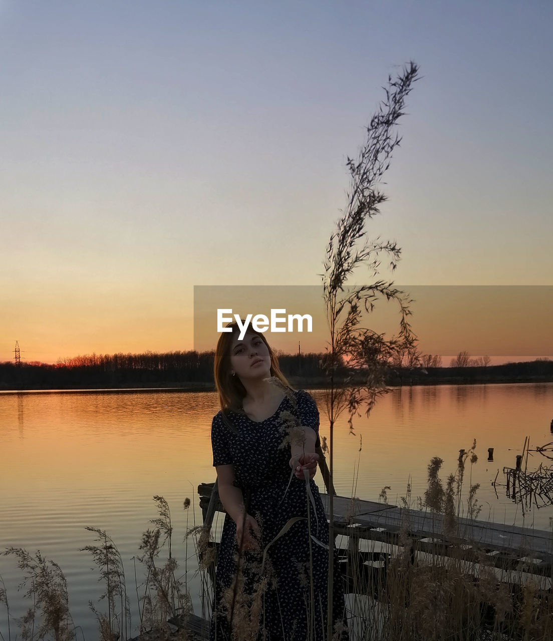 Portrait of woman by lake against sky during sunset