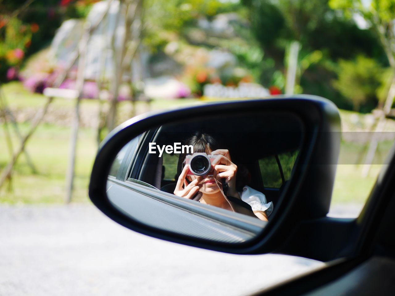 Reflection of woman photographing in side-view mirror