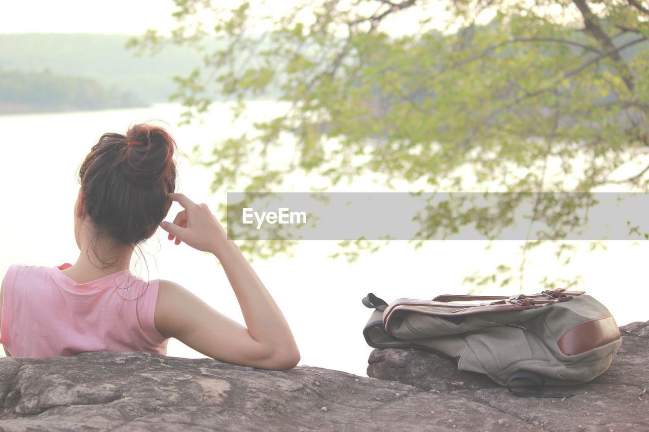 Rear view of woman sitting with bag by rock