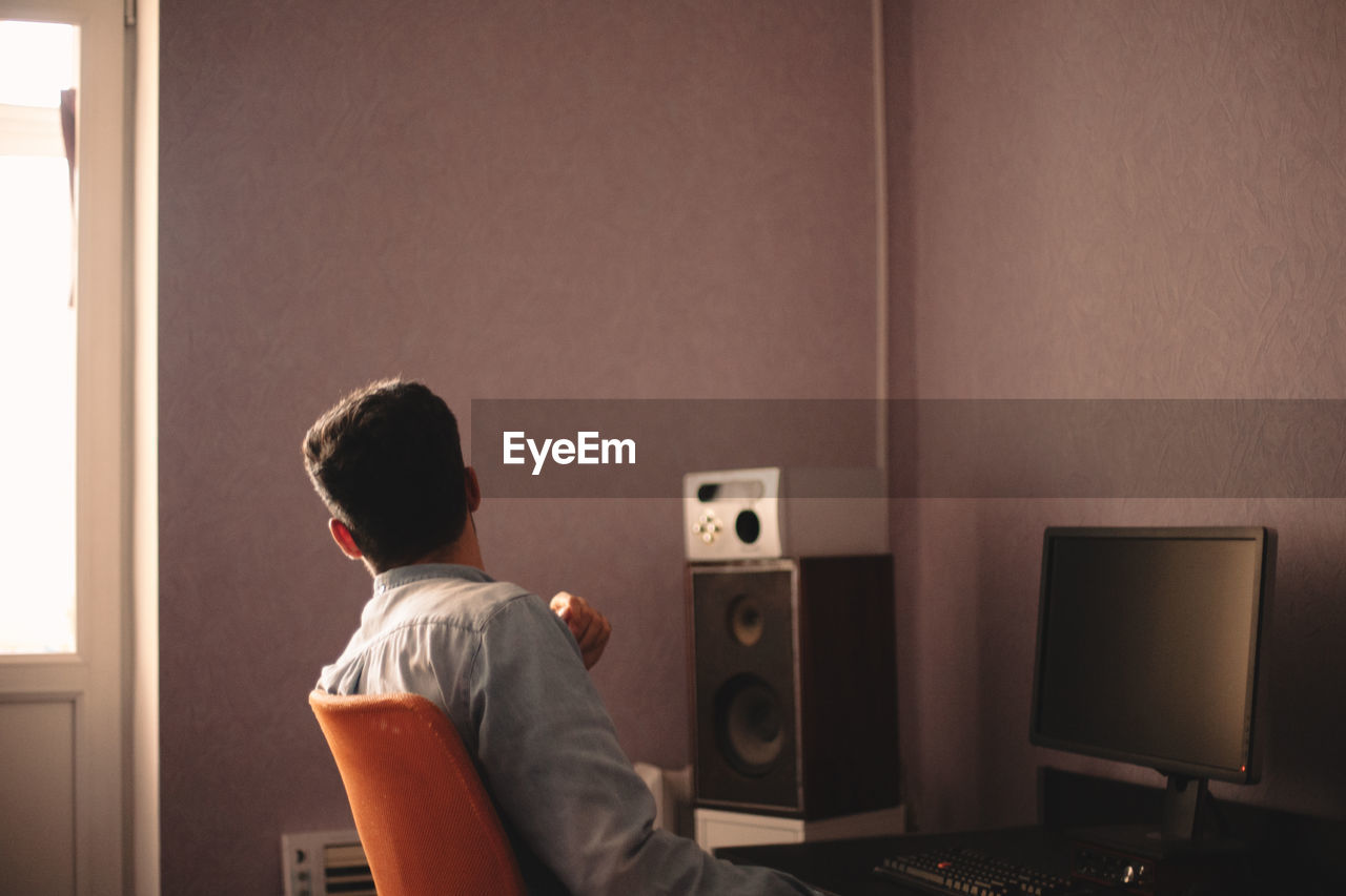 Man looking through window while sitting by desktop computer