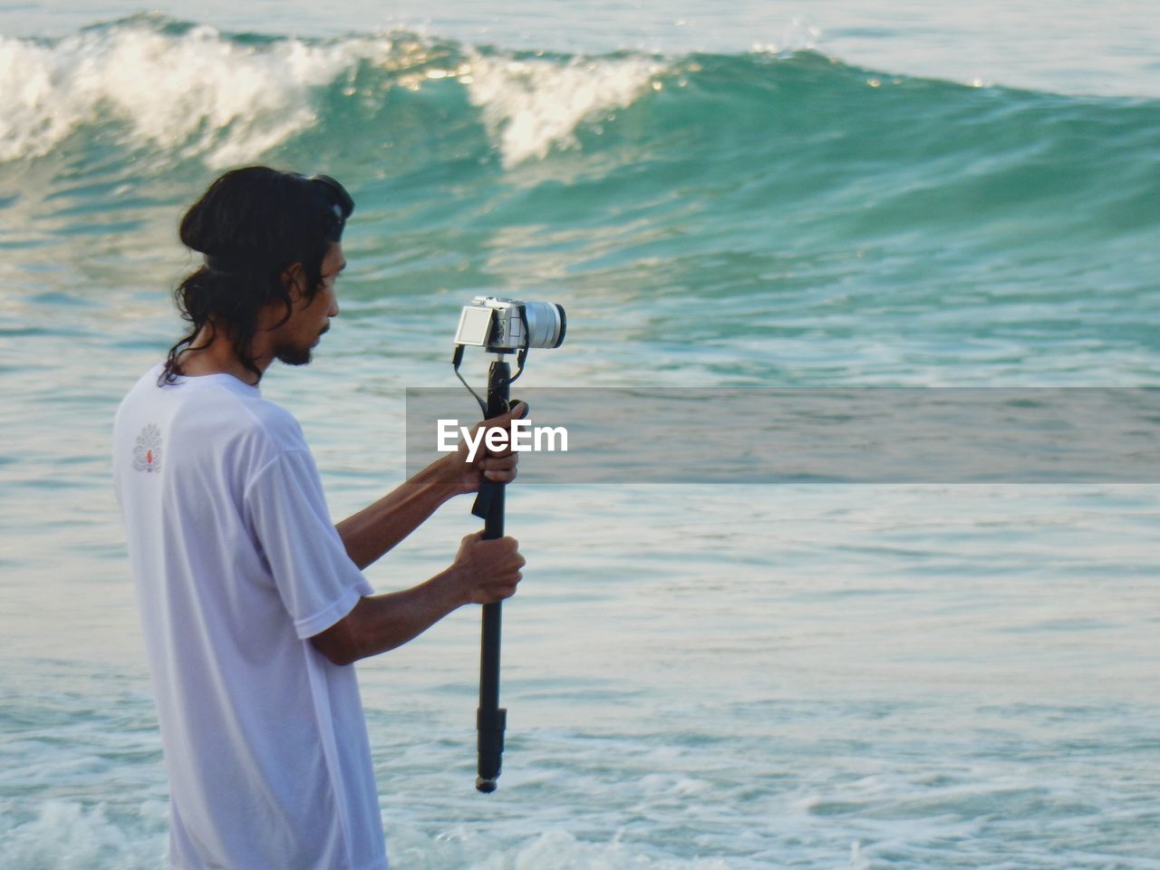 Young man photographing with camera on monopod while standing at seashore