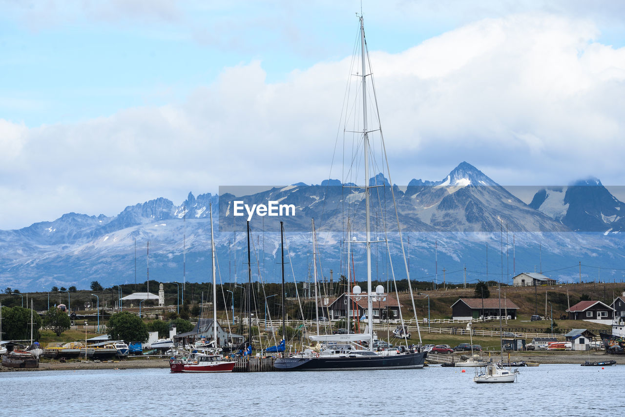 SAILBOATS MOORED IN HARBOR AGAINST MOUNTAINS