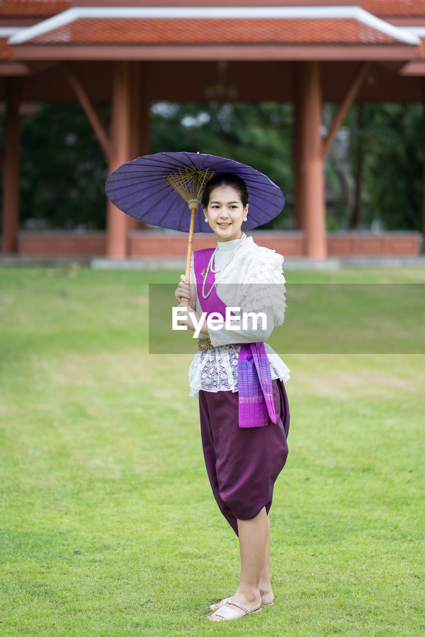 Portrait of smiling woman holding umbrella while standing on land