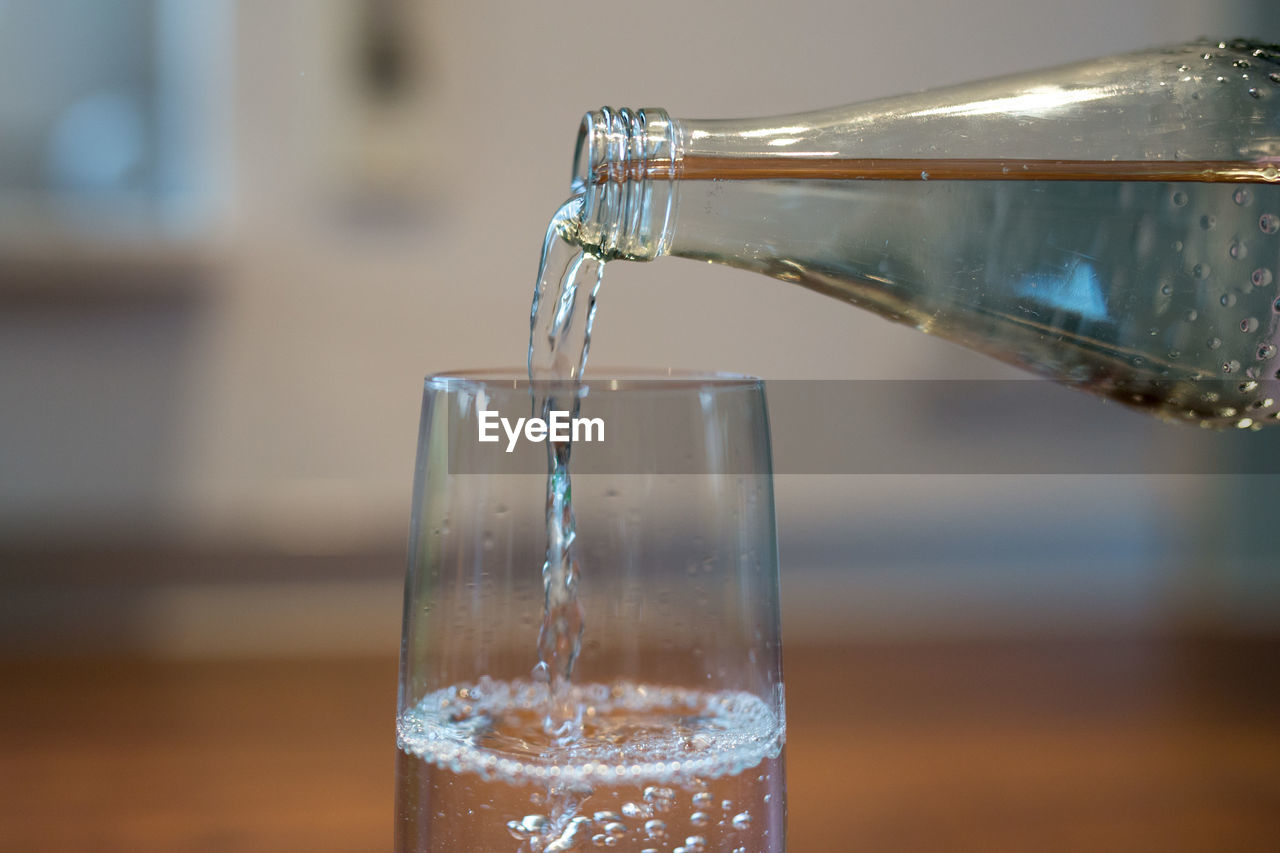 Bottle pouring water in glass on table